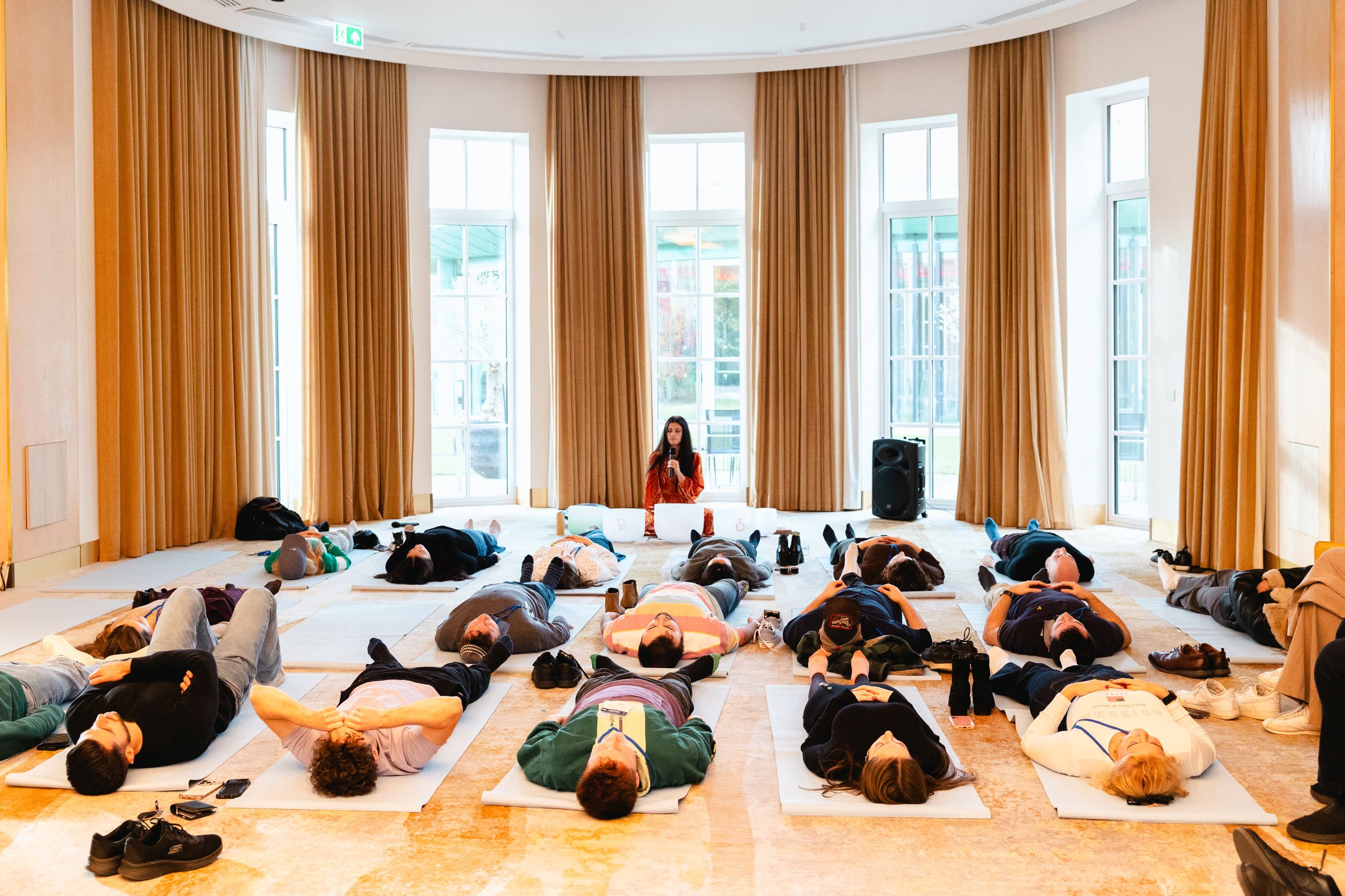 Harriet Emily leading a sound bath for a room of guests lying on mats in a grand ballroom
